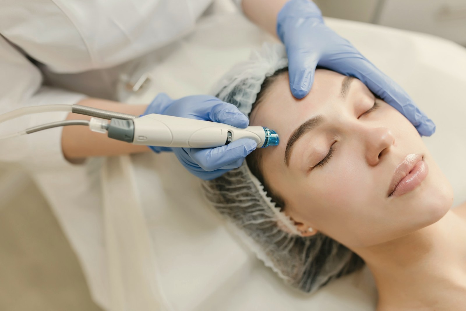 Aesthetic device handpiece drawn across a patient cheek during a machine facial
