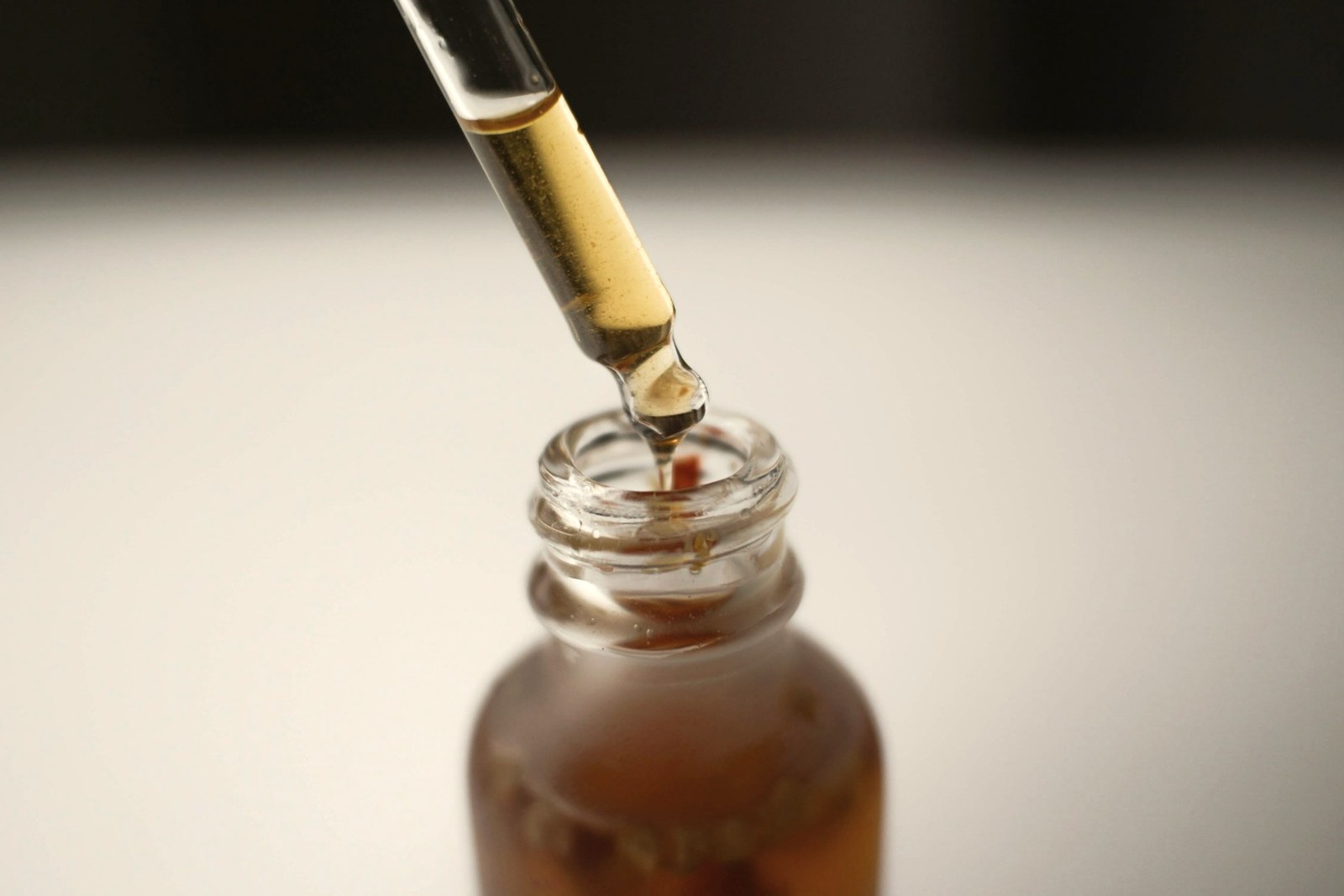 A glass pipette dispensing serum into an amber bottle