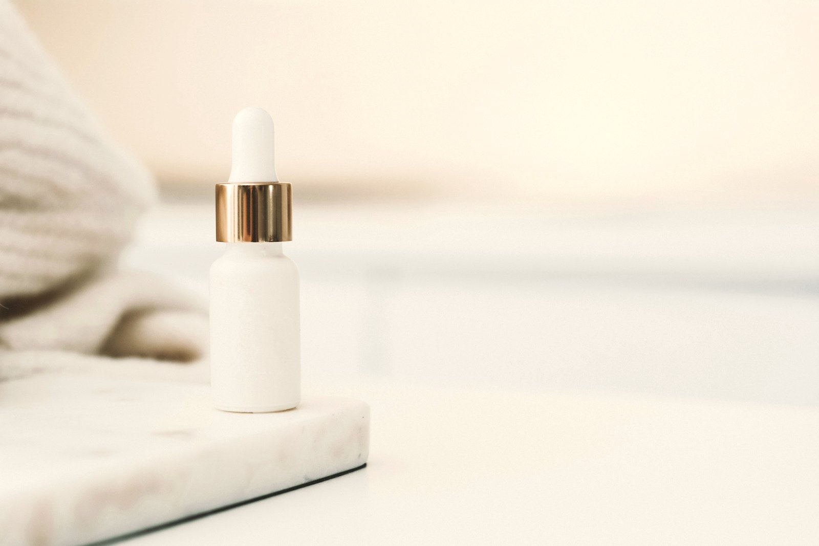 An unbranded white dropper serum bottle on a pale marble surface