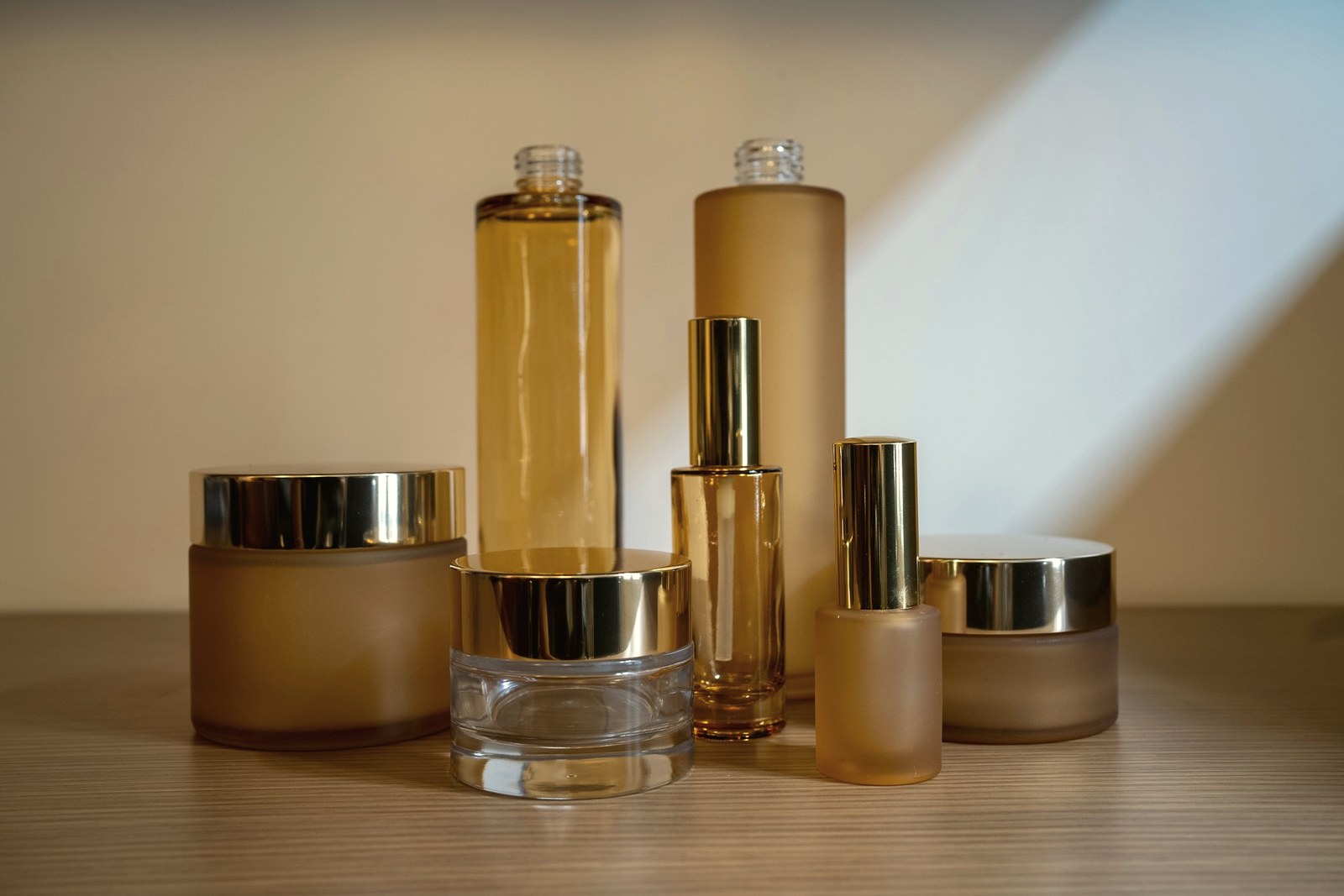 Frosted amber and gold skincare bottles and jars arranged on a wooden surface